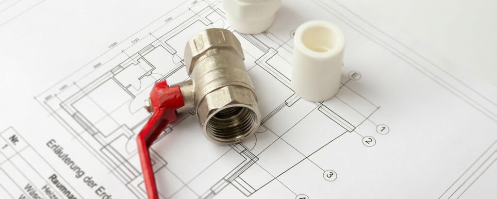 Foto von einem Metallwasserhahn mit rotem Griff und zwei weißen Kunststoffrohren auf einer Architektenzeichnung.